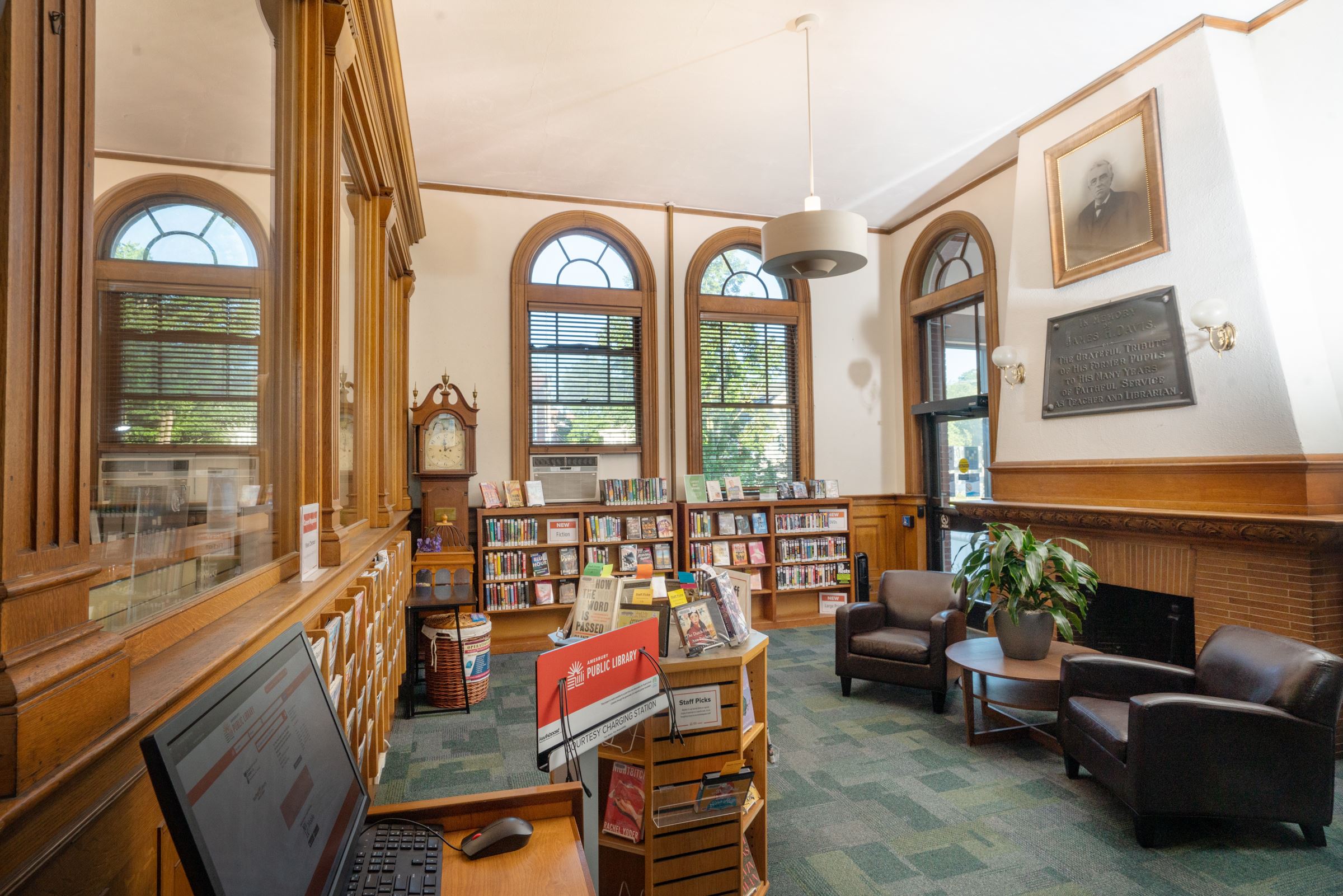 view of the New Room showing catalog station, staff picks display, new magazines, new fiction & LP, building entrance facing parking lot, & two armchairs